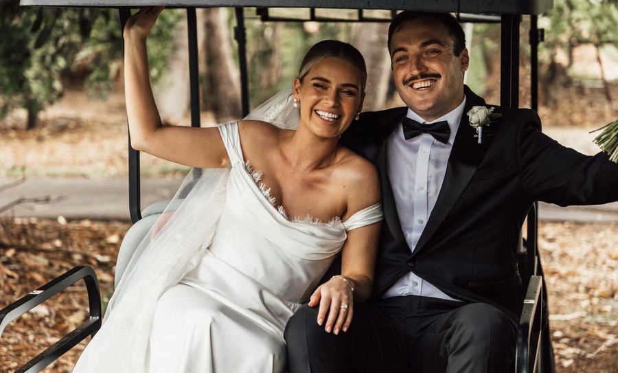A newlywed couple in a golf cart laughing with one another