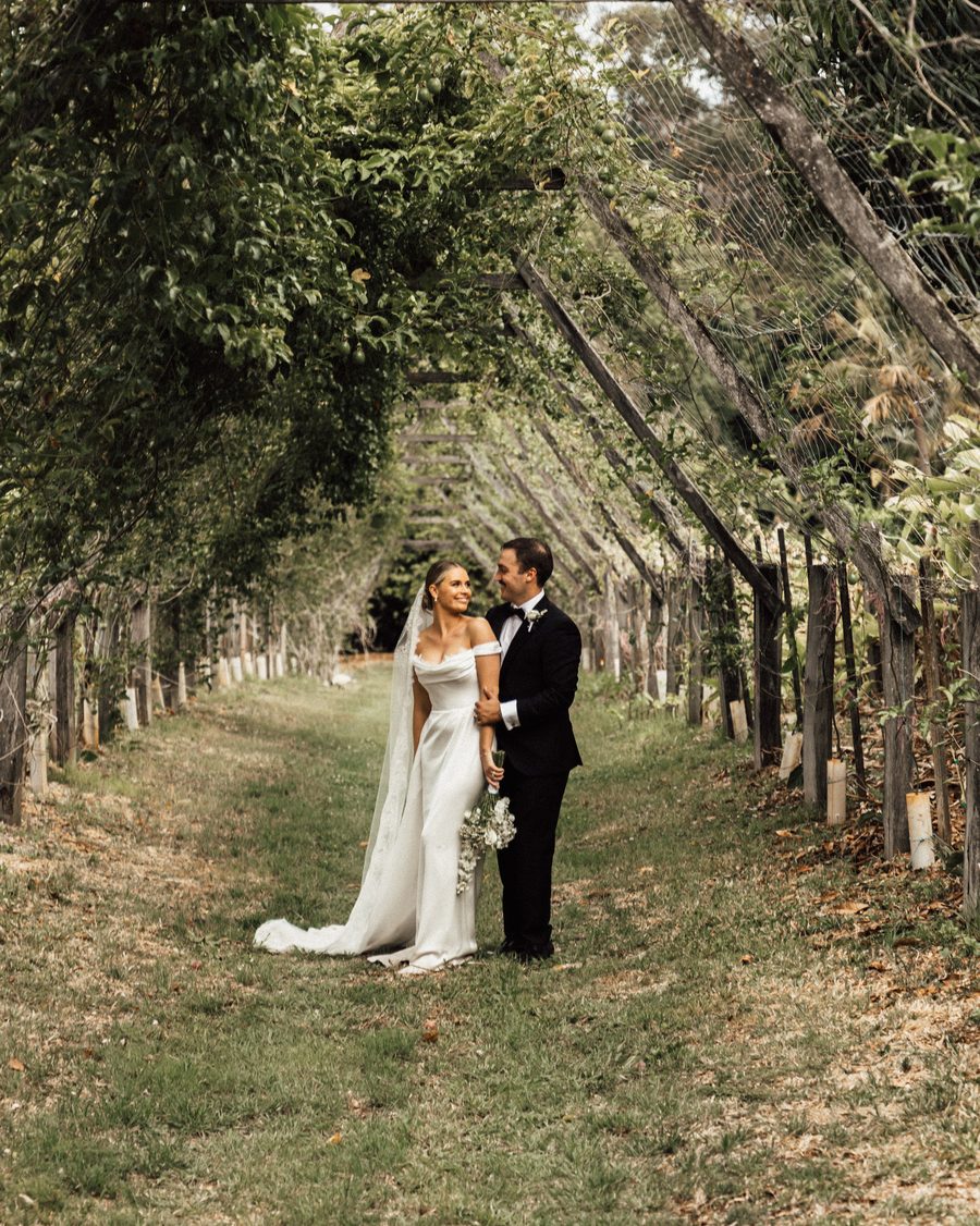 A bride and groom holding hands under passionfruit vines