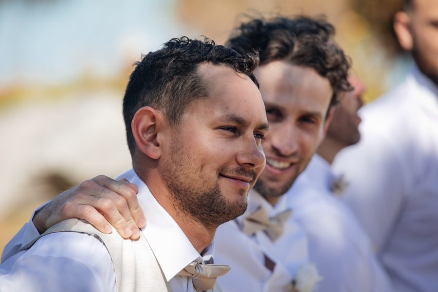 A Groom and his groomsman smiling as a bride walks down the aisle