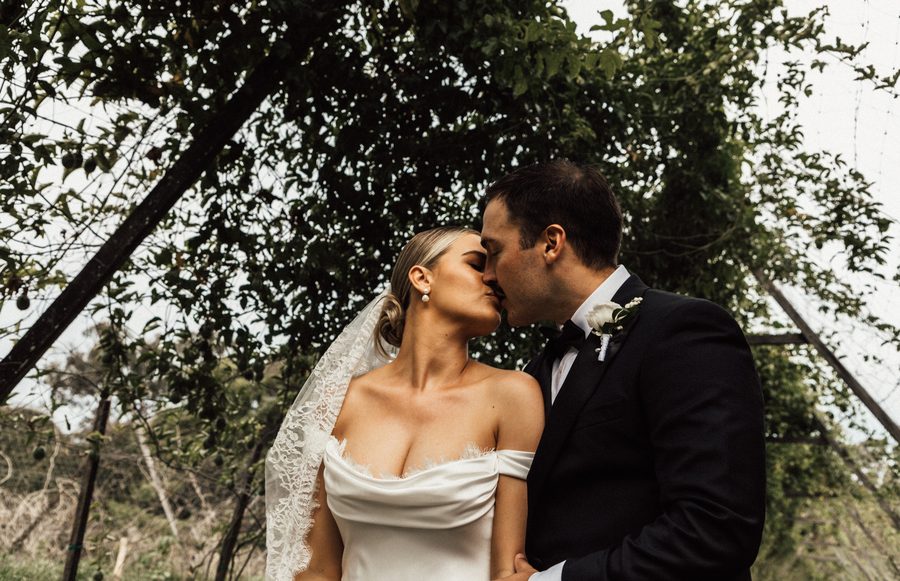 A newlywed couple sharing a kiss beneath a vineyard